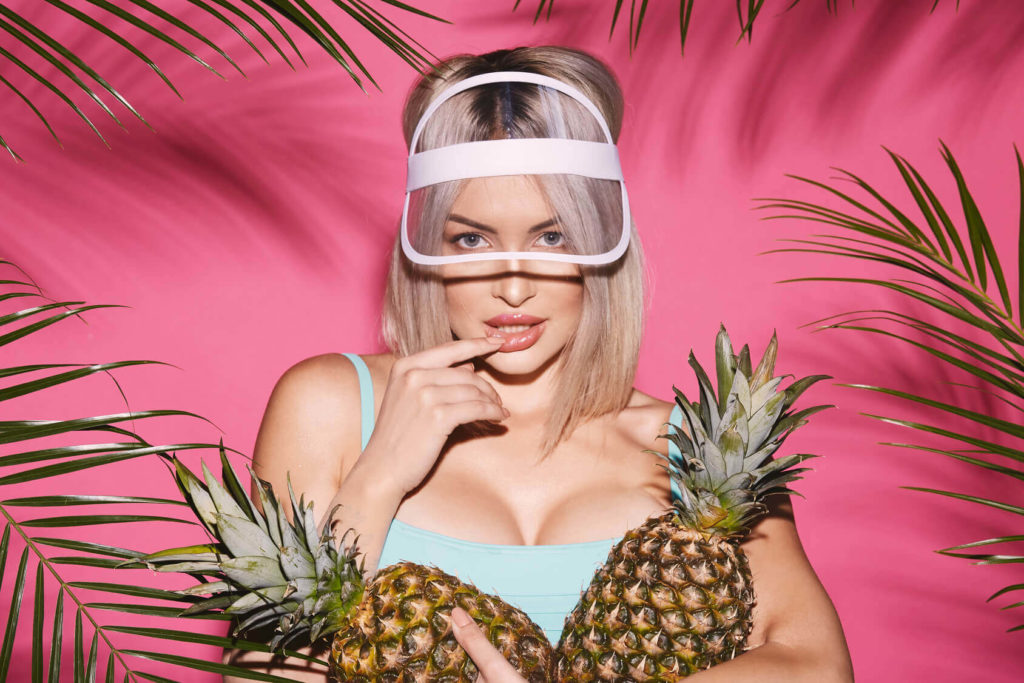 Hot girl with pineapples with a sensual look on her face and funny looking cap.