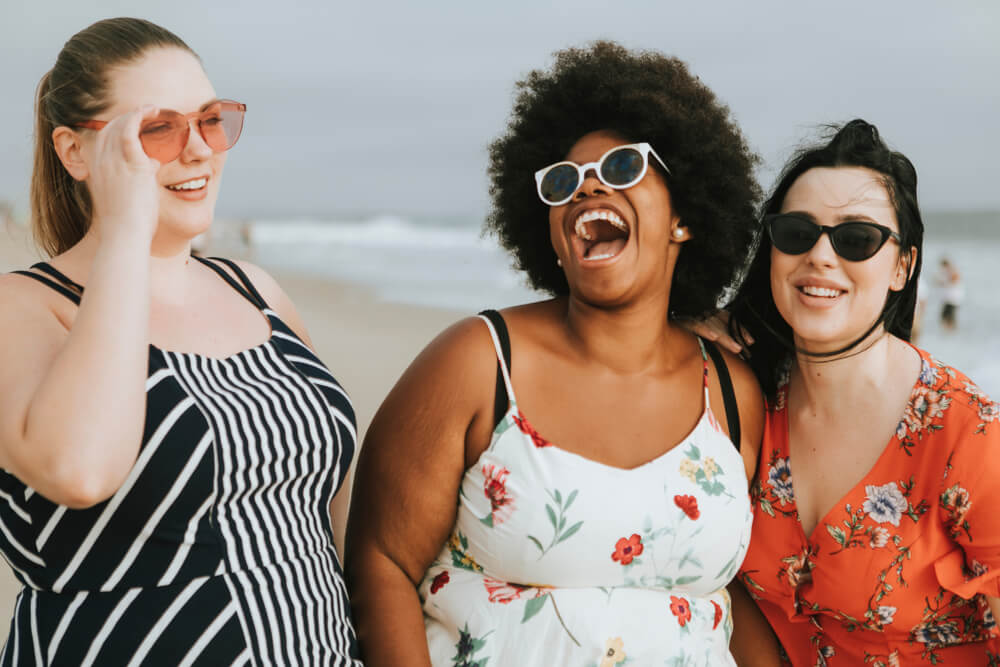3 beautiful curvy women from different ethnicities backgrounds laughing on the beach