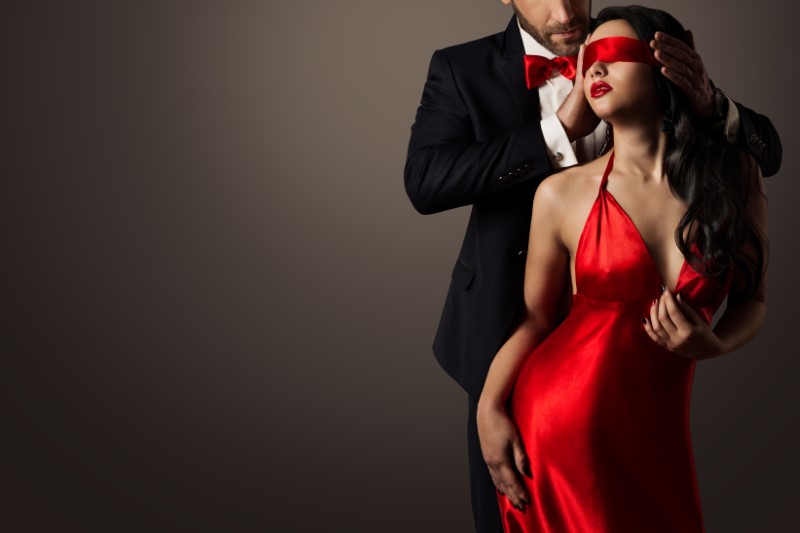 Women in sexy red silk dress being blindfolded by her date
