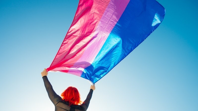 Woman holding bisexual flag high up in the sky