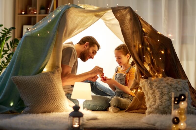 Single dad is having a tea party with his daughter in self-made tent at home