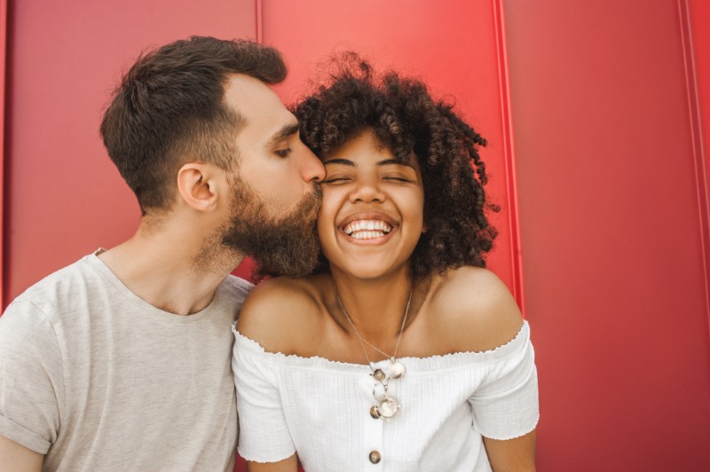 Man with beard kisses his joyful bpoc girlfriend on the cheek