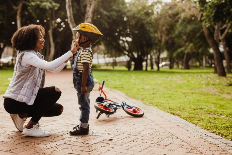 Single mom helps her son with his helmet while he learns how to drive a bike